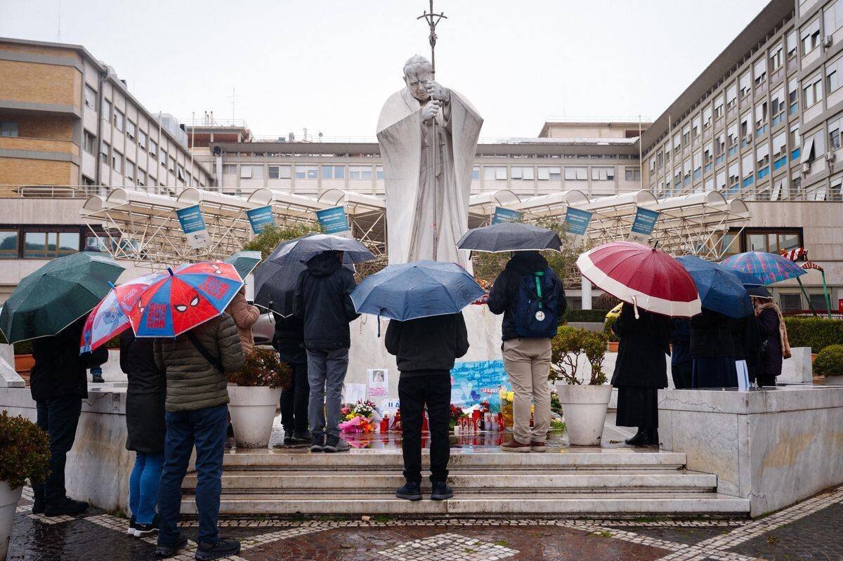 Des personnes prient sous la pluie devant la statue de Jean-Paul II à l’hôpital Gemelli à Rome, où le pape François est hospitalisé avec une pneumonie, le 1ᵉʳ mars 2025.