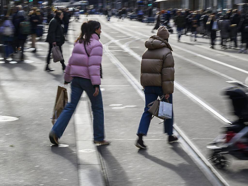 Des gens traversent la Bahnhofstrasse à Zurich lors d'une journée animée, entourés de sacs d'achats et de passants.
