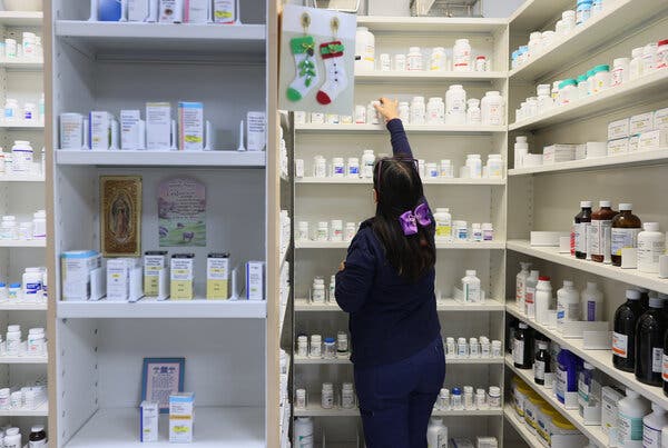 Un technicien en pharmacie atteint une bouteille de médicaments sur une étagère haute.