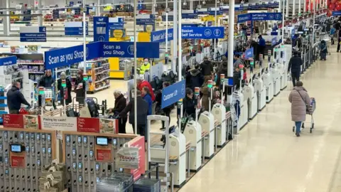 Clients faisant leurs courses dans un Tesco avec des panneaux Scan as you Shop