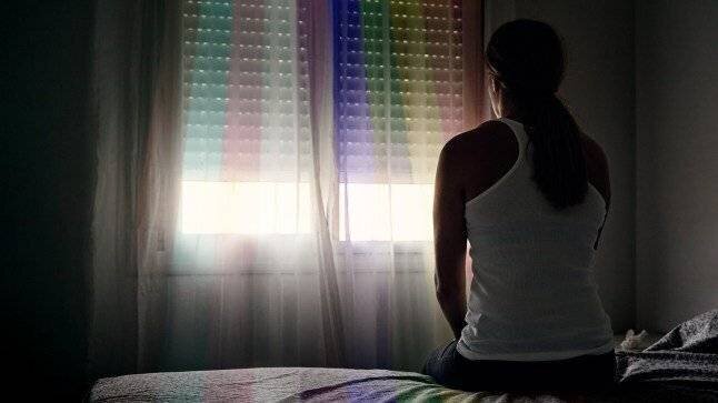 Vue arrière d'une femme abusée assise sur son lit regardant par la fenêtre.