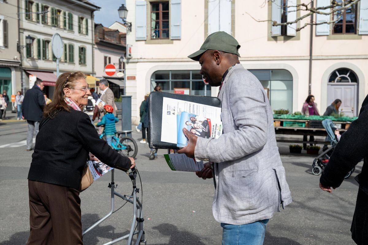 Personnes discutant près des stands pour les élections municipales 2025 à Carouge, Suisse, sur la place du Marché.
