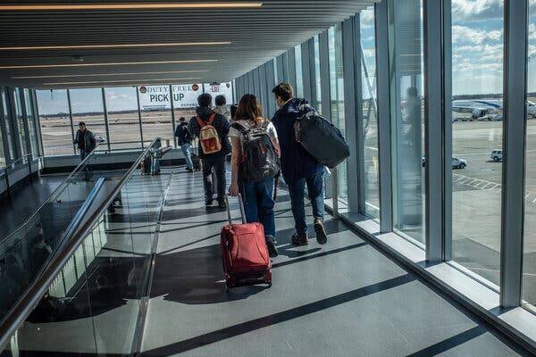 Des personnes marchant dans un aéroport devant de grandes fenêtres avec vue sur le tarmac.