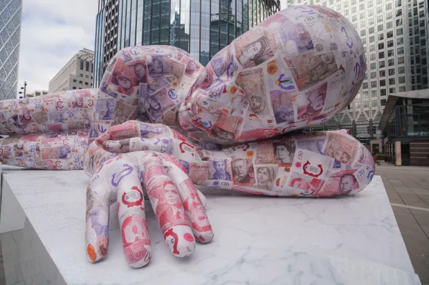 Sculpture d'un géant endormi recouvert de billets de banque britanniques.