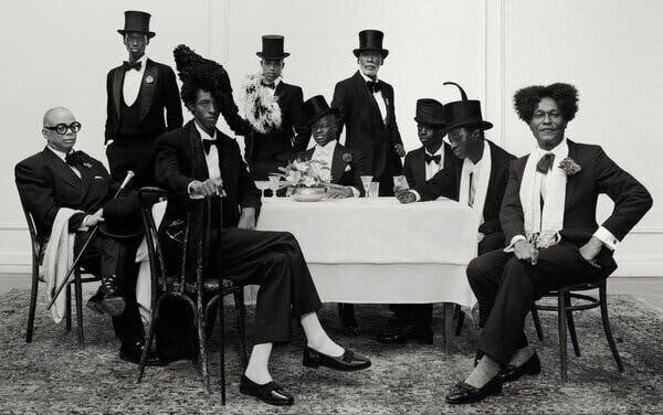 Un portrait de groupe en noir et blanc montrant neuf hommes noirs élégamment habillés autour d'une table.