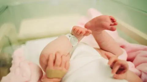 Un nouveau-né dans un service hospitalier - seuls les pieds du bébé et une étiquette de sécurité sont visibles.