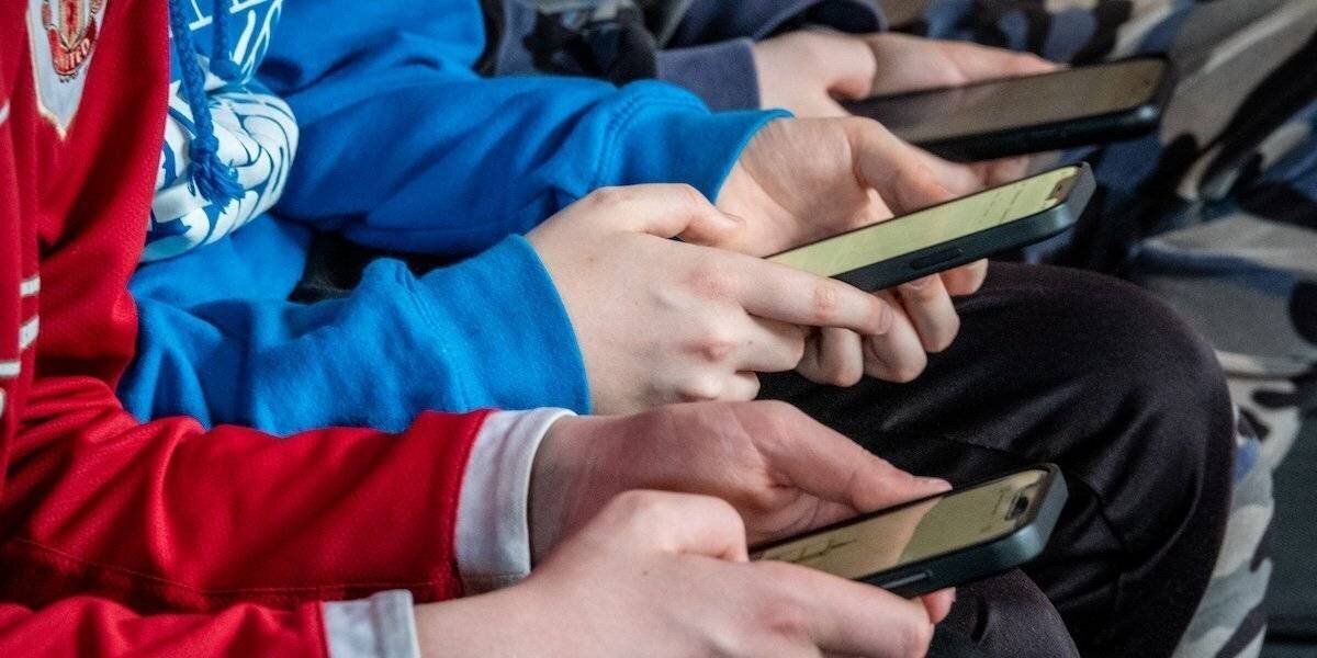 Une photo qui montre les mains de trois garçons assis près d'eux tout en utilisant leurs smartphones