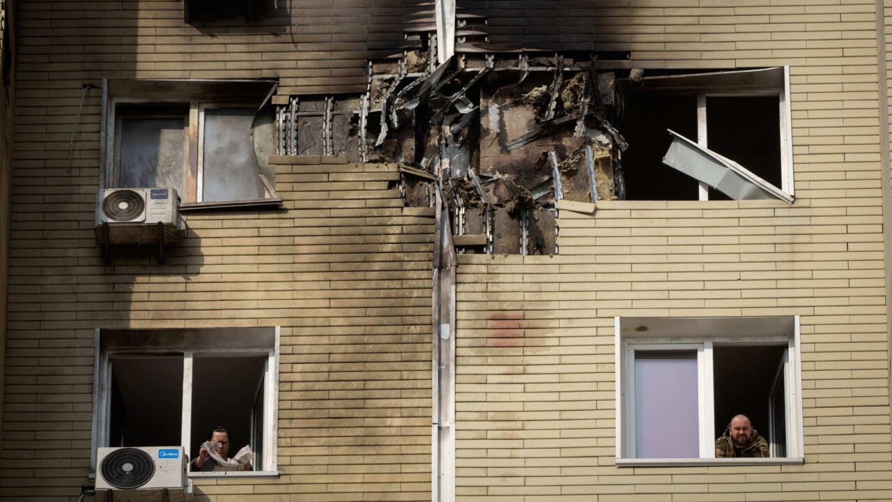 Un habitant observe son voisin nettoyer son appartement endommagé après l'attaque de drones de nuit à Kyiv, Ukraine, le 23 mars 2025.