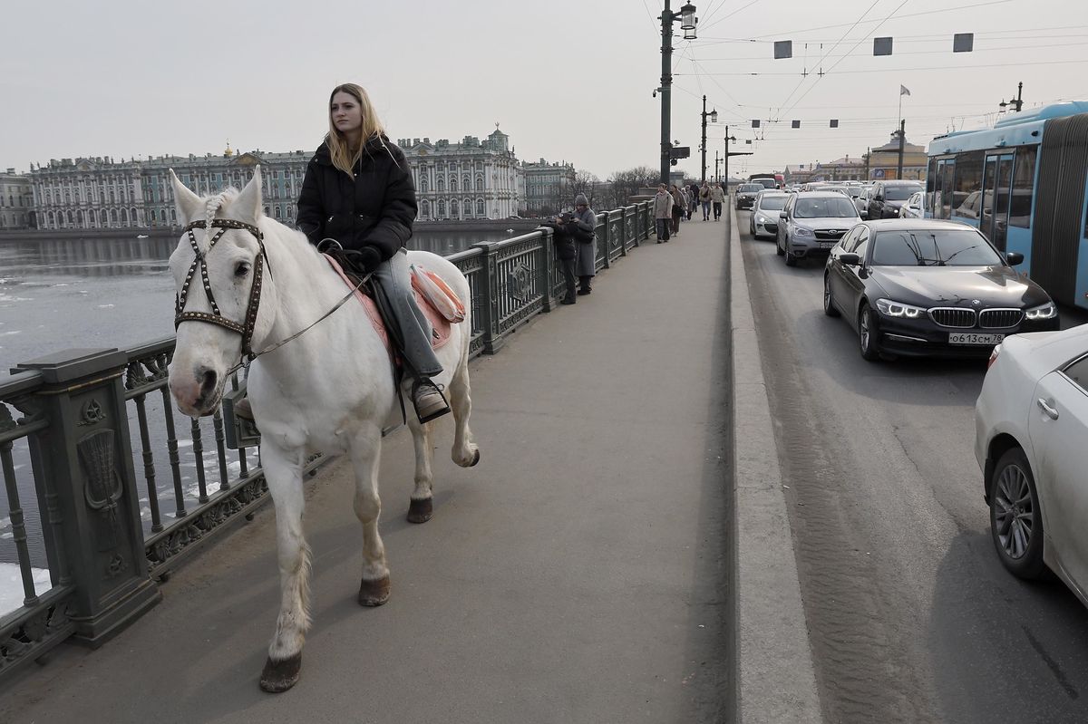 Une femme chevauchant un cheval blanc sur le pont Dvortsovy à Saint-Pétersbourg, Russie, par une journée ensoleillée.