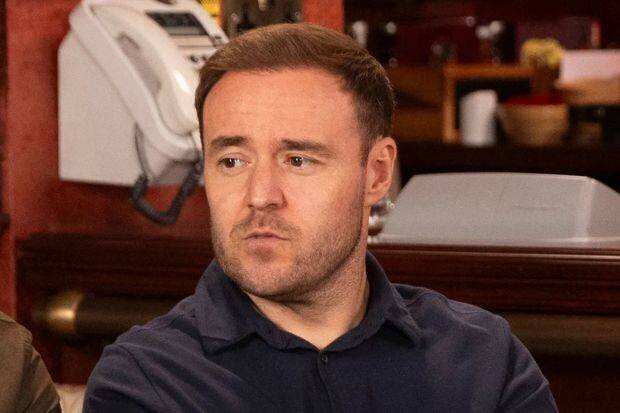 Cinq hommes assis autour d'une petite table dans un pub, participant à une compétition de fléchettes