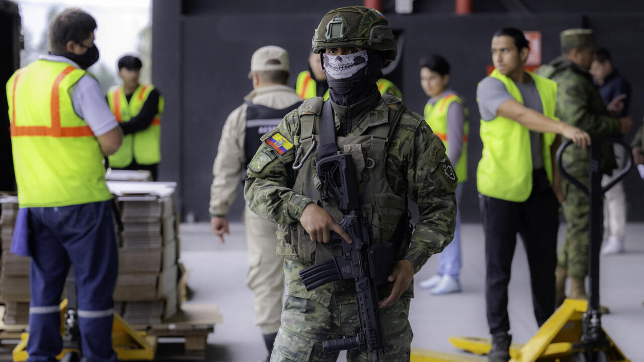 Un soldat masqué monte la garde devant des membres de la Commission électorale qui préparent le matériel de vote à la veille de l'élection présidentielle en Equateur, le 12 avril 2025 à Quito