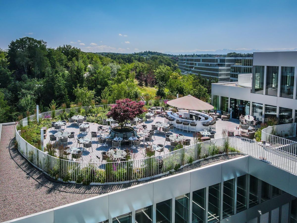 Terrasse sur le toit d'un bâtiment moderne avec tables et chaises, entourée d'arbres verts et vue panoramique sur le paysage
