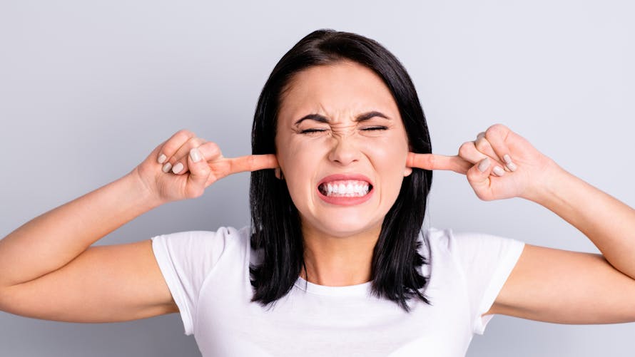 Femme agacée se bouche les oreilles avec les doigts en fermant les yeux et la bouche