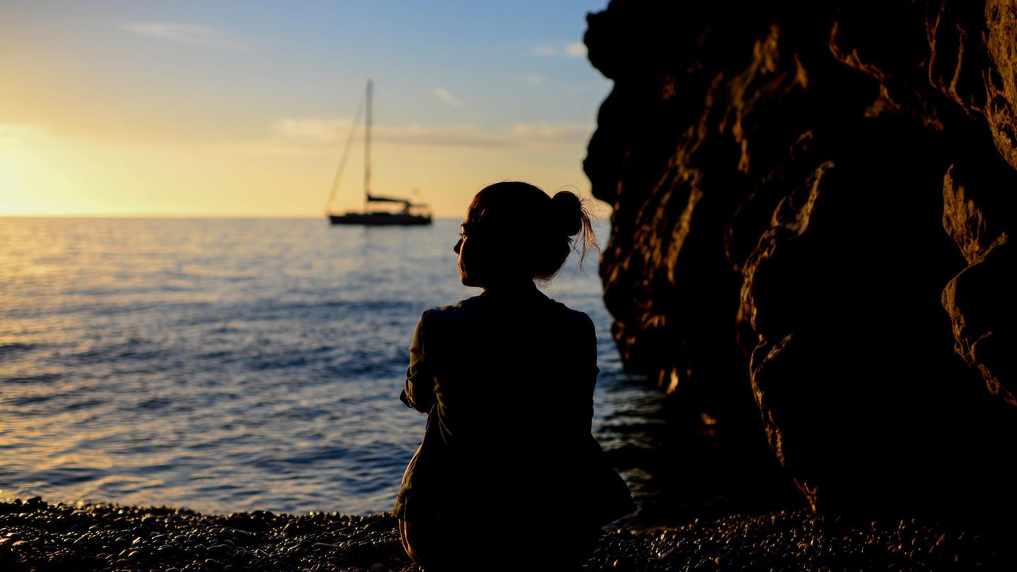Femme pensive assise au coucher du soleil au bord de la mer
