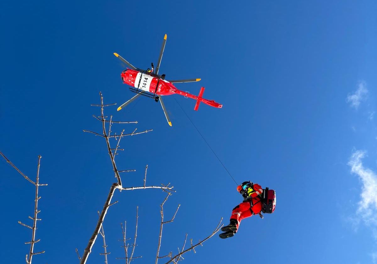 Hélicoptère de sauvetage Rega avec sauveteur en tenue rouge suspendu à la treuillée