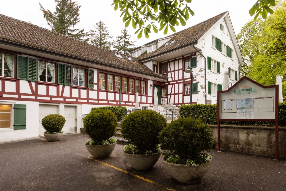 Le restaurant Muggenbühl à Wollishofen, Zürich avec sa structure traditionnelle à colombages, grande terrasse et aire de jeux.