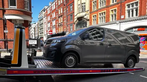 Fourgon gris chargé sur un camion de remorquage dans une rue de Londres