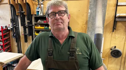 Steve Davies appuyé sur un établi dans un atelier de menuiserie