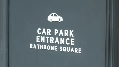 Panneau d’entrée du parking Rathbone Square avec icône de voiture blanche sur fond sombre