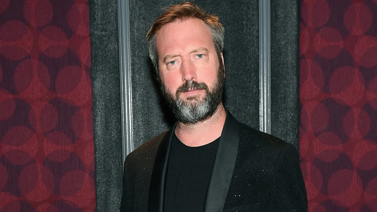 Gros plan de Tom Green portant une chemise noire et un blazer.
