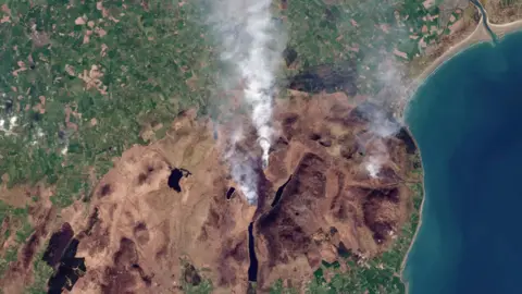 Image satellite montrant une vaste zone de végétation brune avec de la fumée visible au Royaume-Uni
