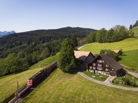Train rouge des Appenzeller Bahnen traversant un paysage vallonné avec une ferme