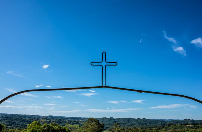 Une croix décorative en métal sur fond de ciel bleu et de paysage vert, à Pelotas, au Brésil.
