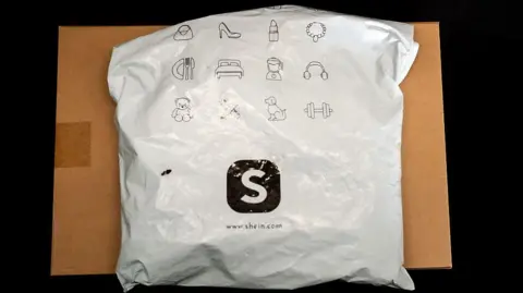 Colis Shein posé sur un carton, emballage blanc avec logo Shein noir