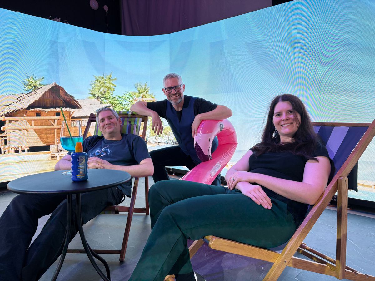 Trois personnes détendues sur des chaises longues devant un écran avec un décor de plage tropicale et un flamant rose gonflable