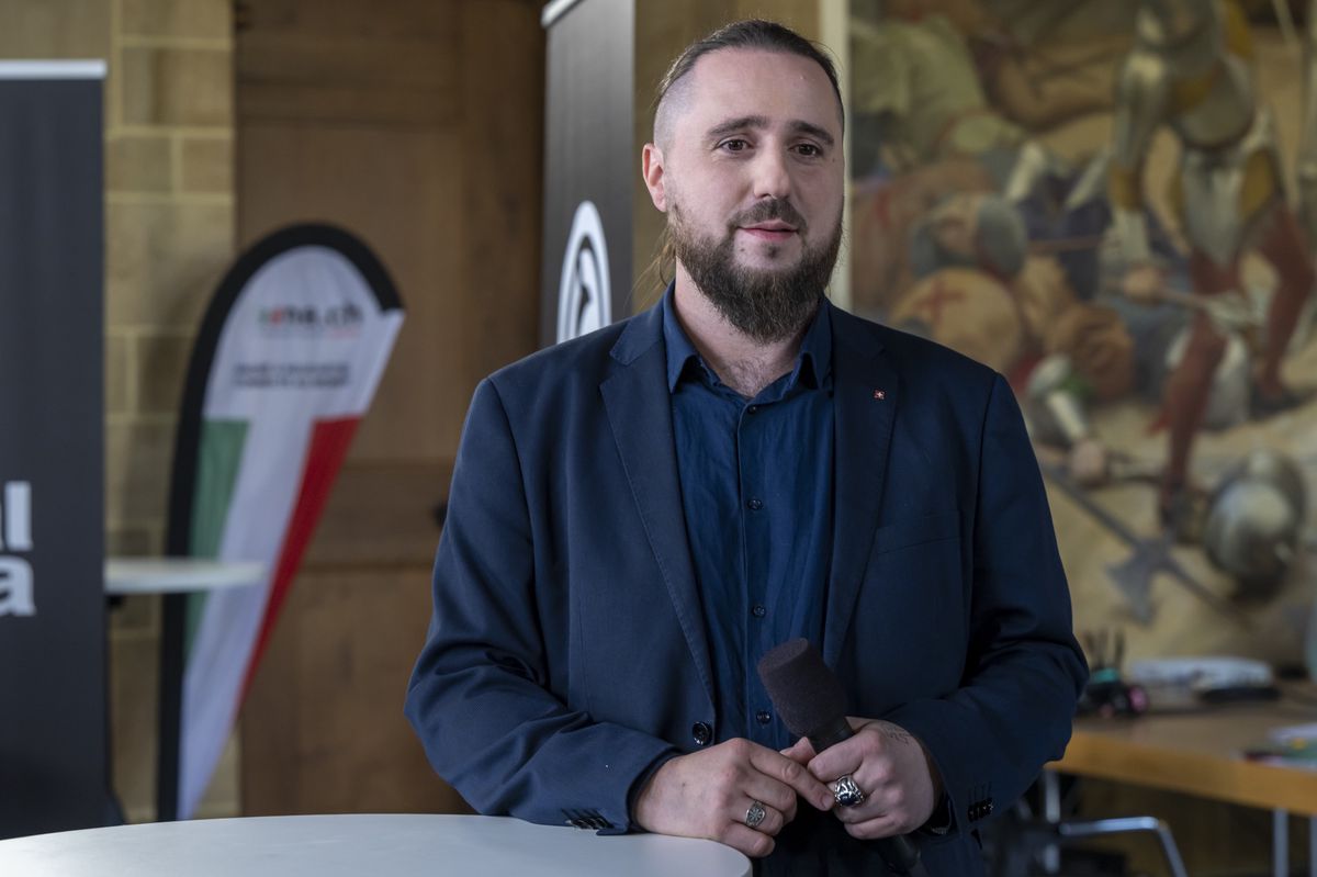 Niels Rosselet-Christ, candidat UDC, s’exprime lors des élections fédérales du 22 octobre 2023 à Neuchâtel, devant une bannière et une peinture murale.
