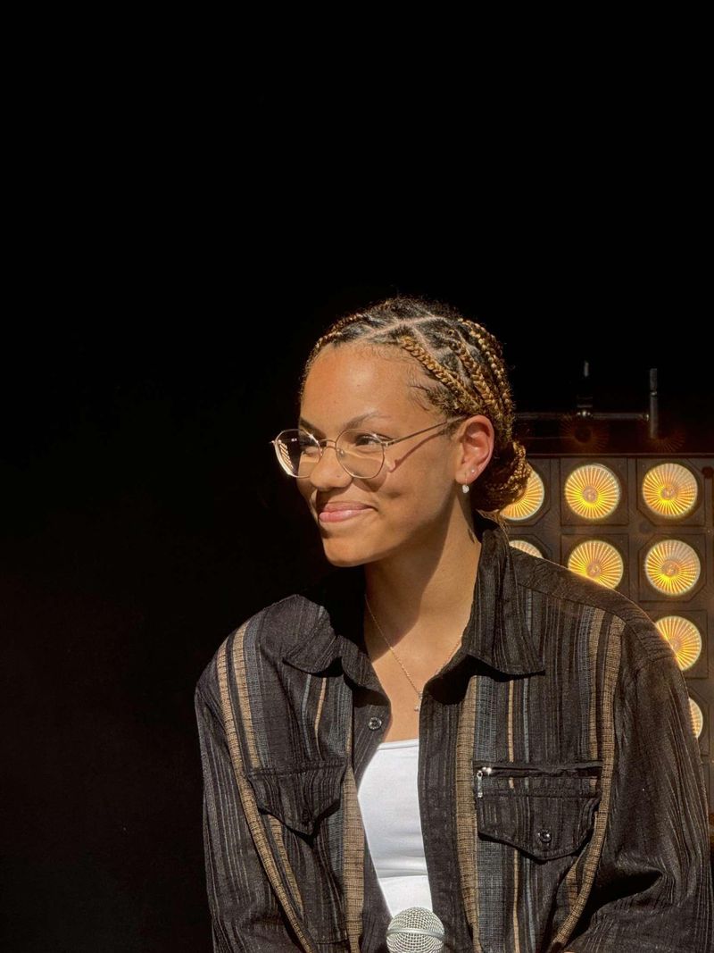La chanteuse Lenda sourit sur scène, tenant un micro, avec un éclairage de projecteurs en arrière-plan.