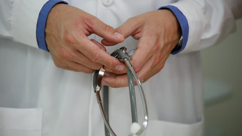 Un professionnel de santé en blouse blanche, avec un stéthoscope dans les mains.