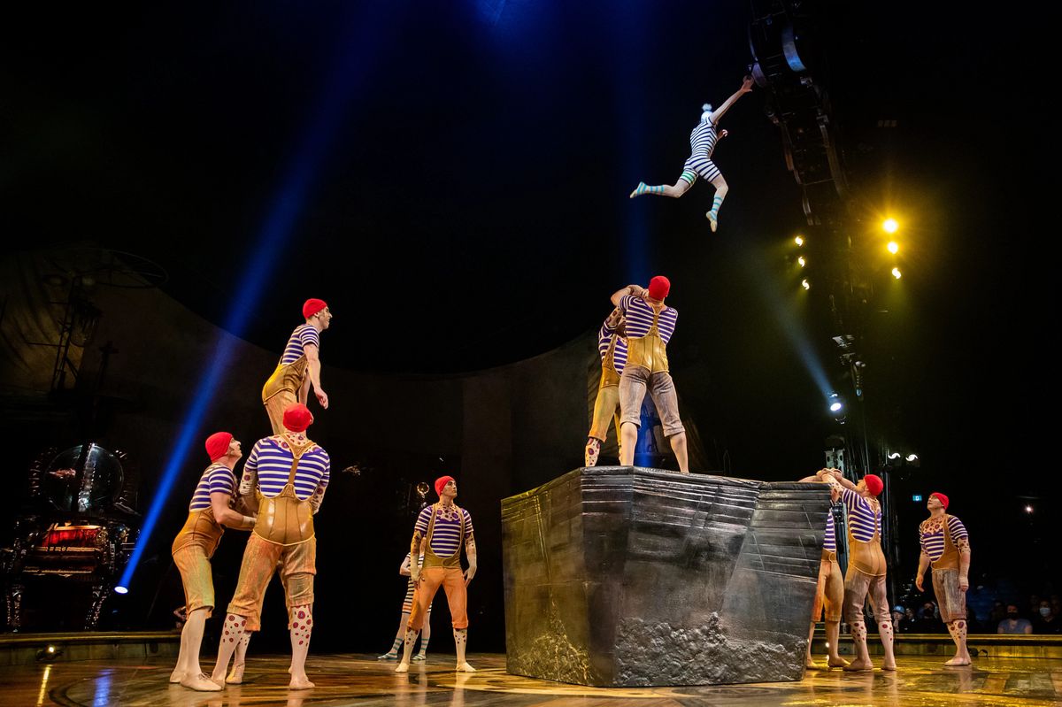Des artistes de cirque en costumes rayés réalisent une performance acrobatique sur une plateforme avec des éclairages de scène.