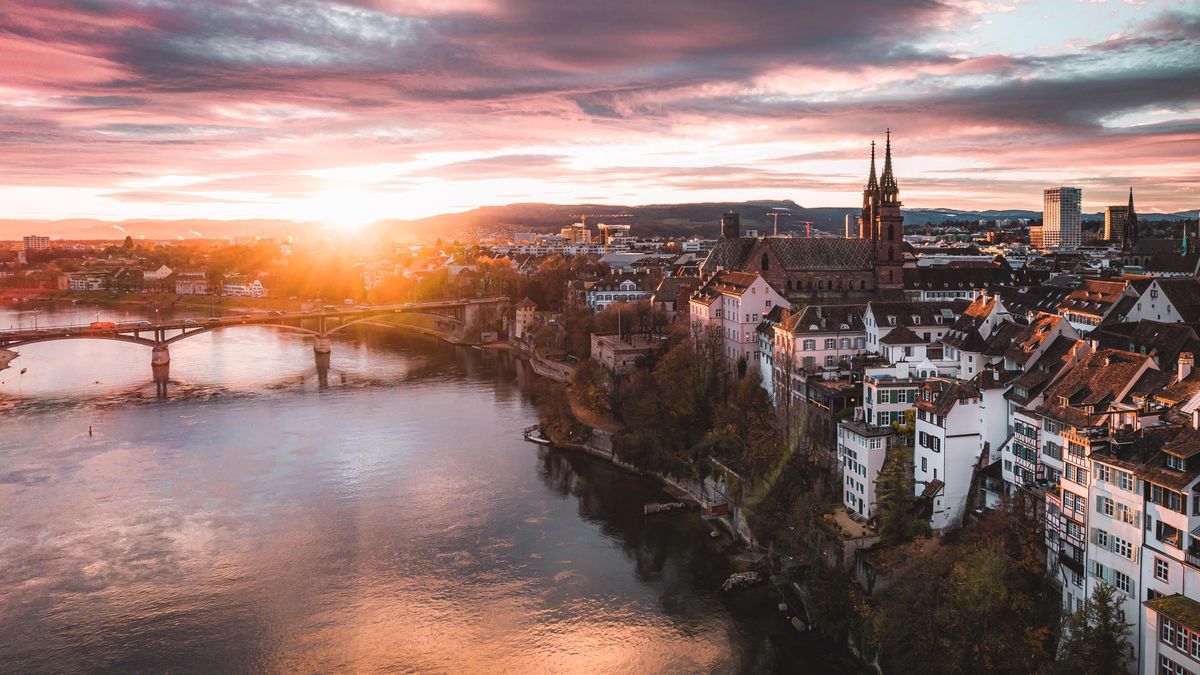 Vue aérienne de Bâle avec le coucher de soleil illuminant le fleuve Rhin et la vieille ville, y compris les structures historiques et le pont.