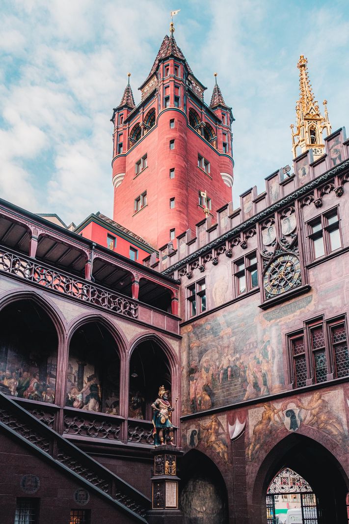 Vue de l’hôtel de ville de Bâle avec sa tour rouge distinctive, des fresques murales et des détails architecturaux gothiques.