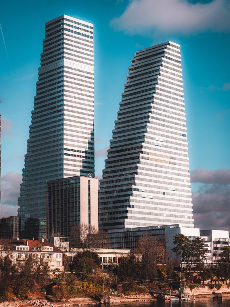 Deux gratte-ciel contemporains avec une architecture en escalier sous un ciel bleu; une base d’immeubles et des arbres au premier plan.
