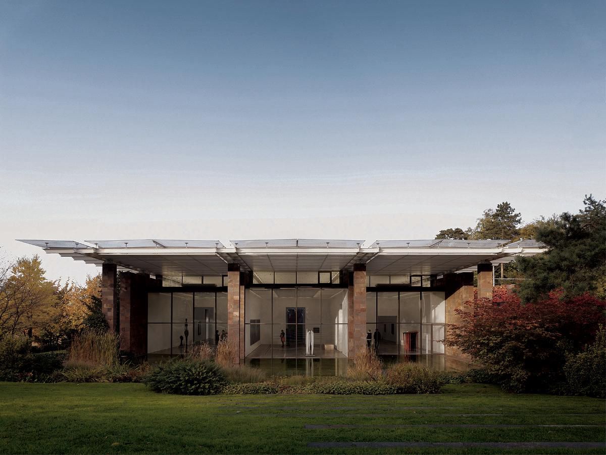 Vue d’un bâtiment moderne entouré de verdure, avec une façade vitrée et un toit plat, sous un ciel dégagé.