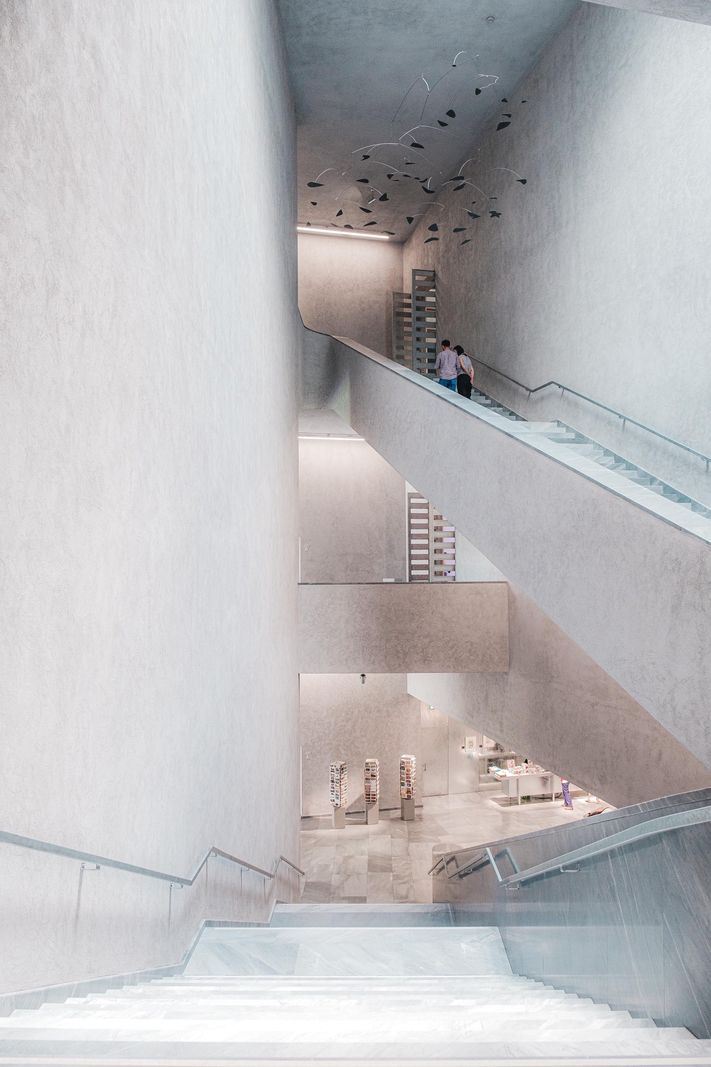 Intérieur moderne d’un bâtiment avec des escaliers et des murs aux surfaces lisses, design épuré et éclairage minimaliste.