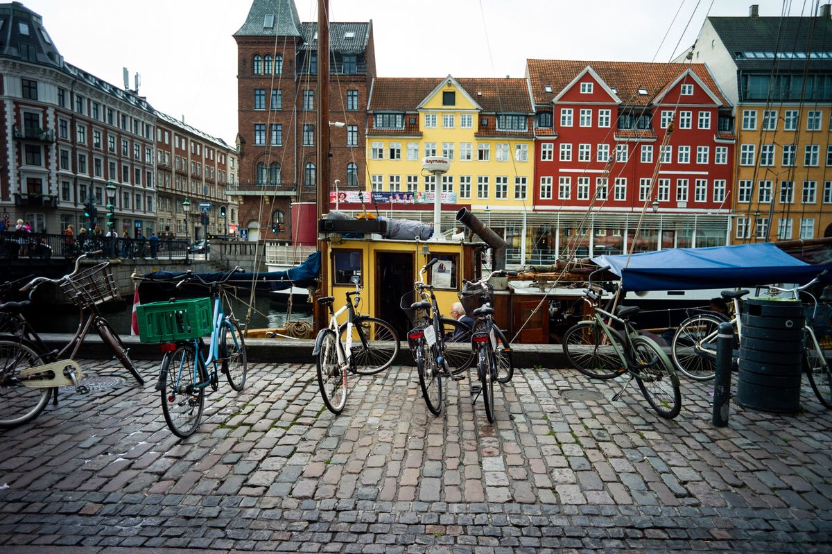 Bateaux en bois historiques amarrés au canal de Nyhavn à Copenhague, entourés de bâtiments colorés du XVIIe siècle, avec des vélos garés au premier plan.
