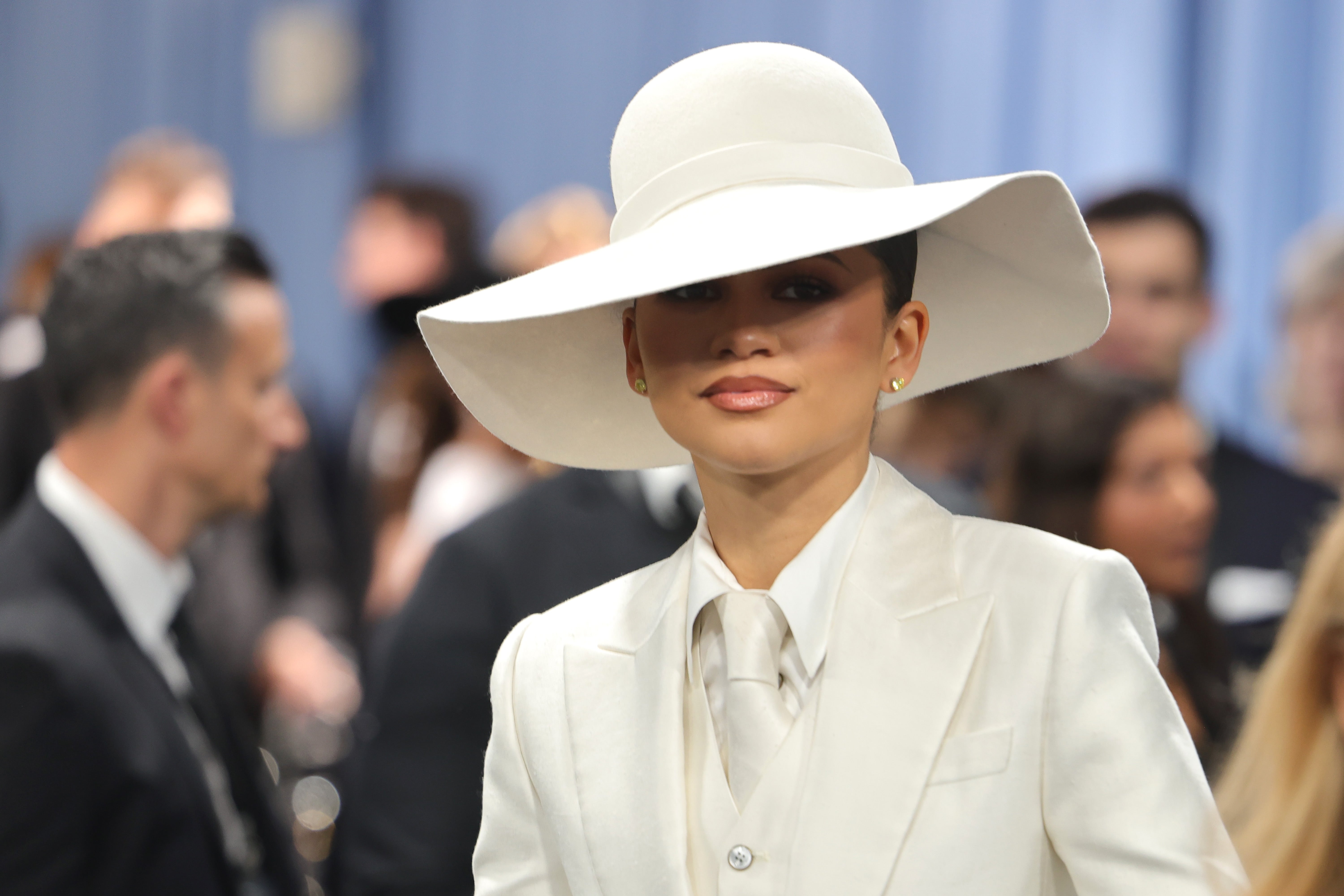 Zendaya cache son visage avec un chapeau à large bord crème