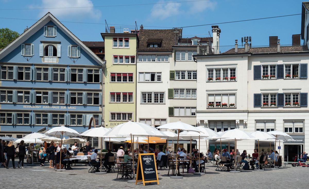 Place Münsterhof à Zurich entourée de bâtiments médiévaux, cafés et restaurants avec des clients sous des parasols.