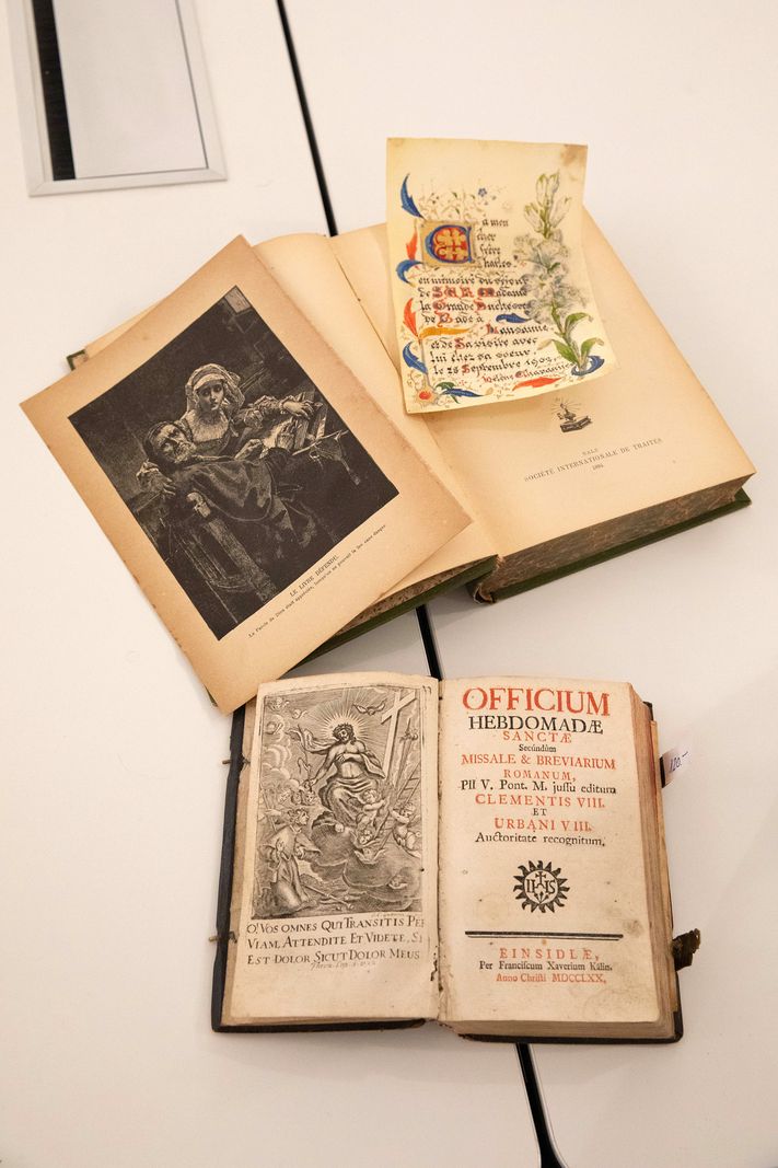 Des livres anciens ouverts exposés dans une galerie d’art à Vevey, comprenant une illustration médiévale et une couverture ornée.