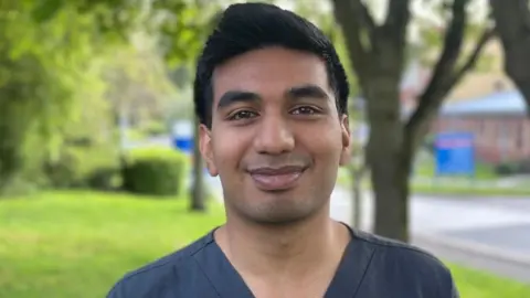 Samren Reddy debout dans un parc avec de l'herbe et des arbres en arrière-plan.