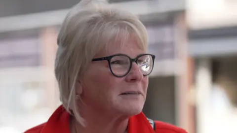 Vanda portant un manteau rouge et des lunettes.