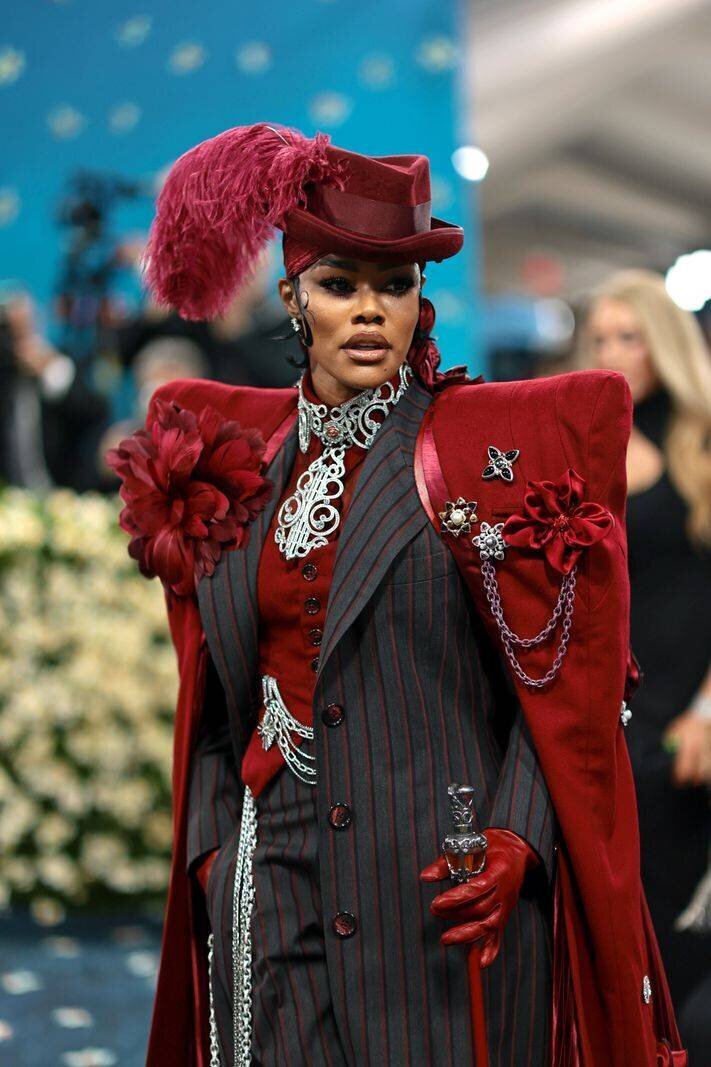 Teyana Taylor au Met Gala 2025, portant un costume rayé rouge avec plumes et broderies, au Metropolitan Museum of Art de New York.