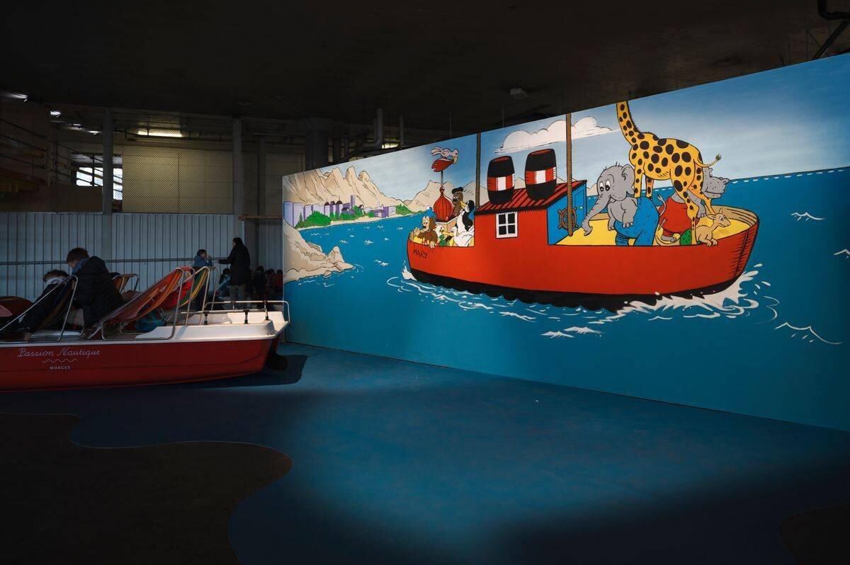 Exposition ’Petzi à l’heure suisse’ au festival BDFIL à Lausanne, montrant une scène colorée avec Petzi et ses amis sur un bateau.