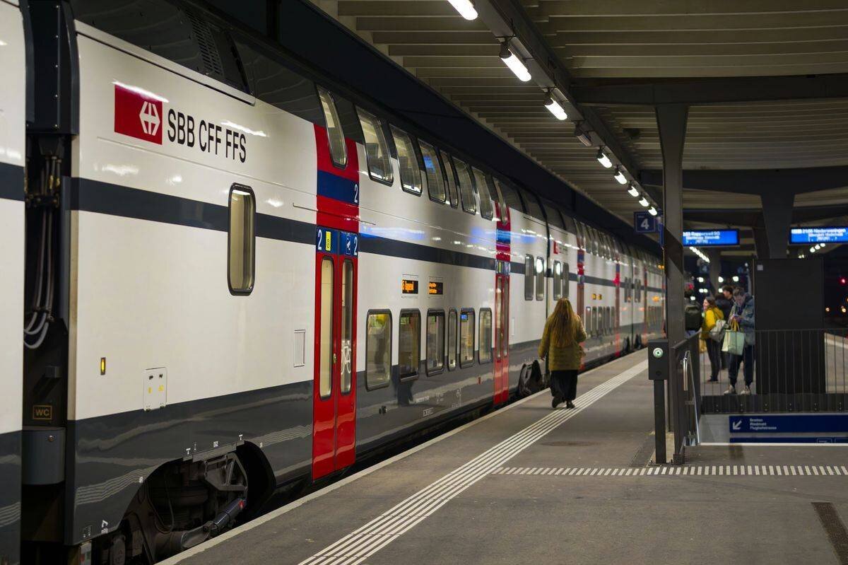 Train SBB CFF FFS arrivant avec des passagers sur le quai de la gare de Rümlang, Zurich, une nuit d’hiver.