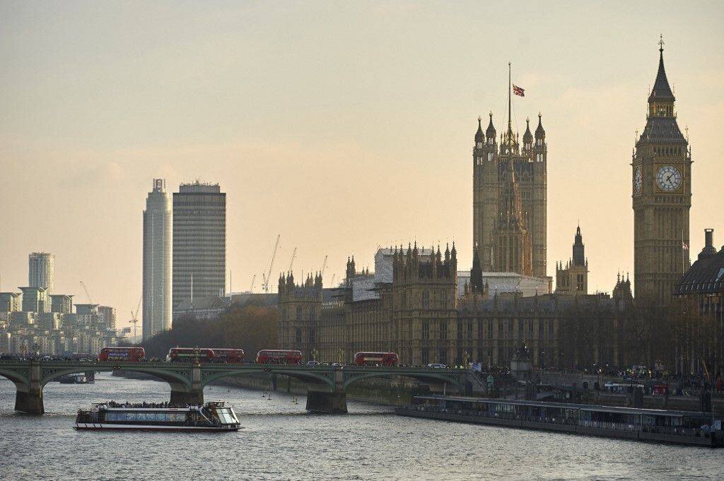 Bus rouges et piétons traversant le pont de Westminster au-dessus de la Tamise. Drapeau britannique en berne sur le palais de Westminster.