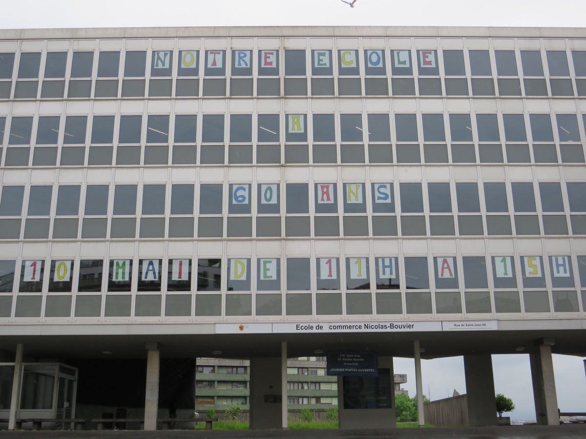 Façade de l’école avec des fenêtres affichant un message coloré : ’NOTRE ÉCOLE A 60 ANS - 10 MAI DE 11H À 15H.'
