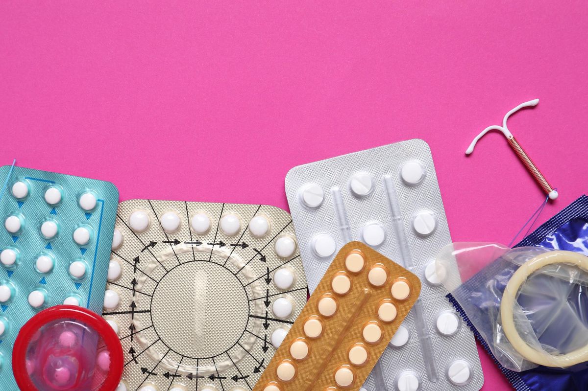 Pilules contraceptives, préservatifs et dispositif intra-utérin sur fond rose, représentant différents moyens de contraception.